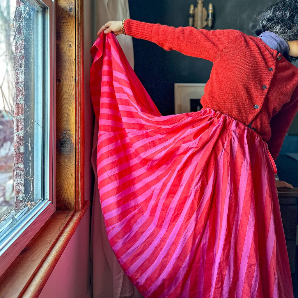 red pink skirt with a red sweater by a window against a grey wall